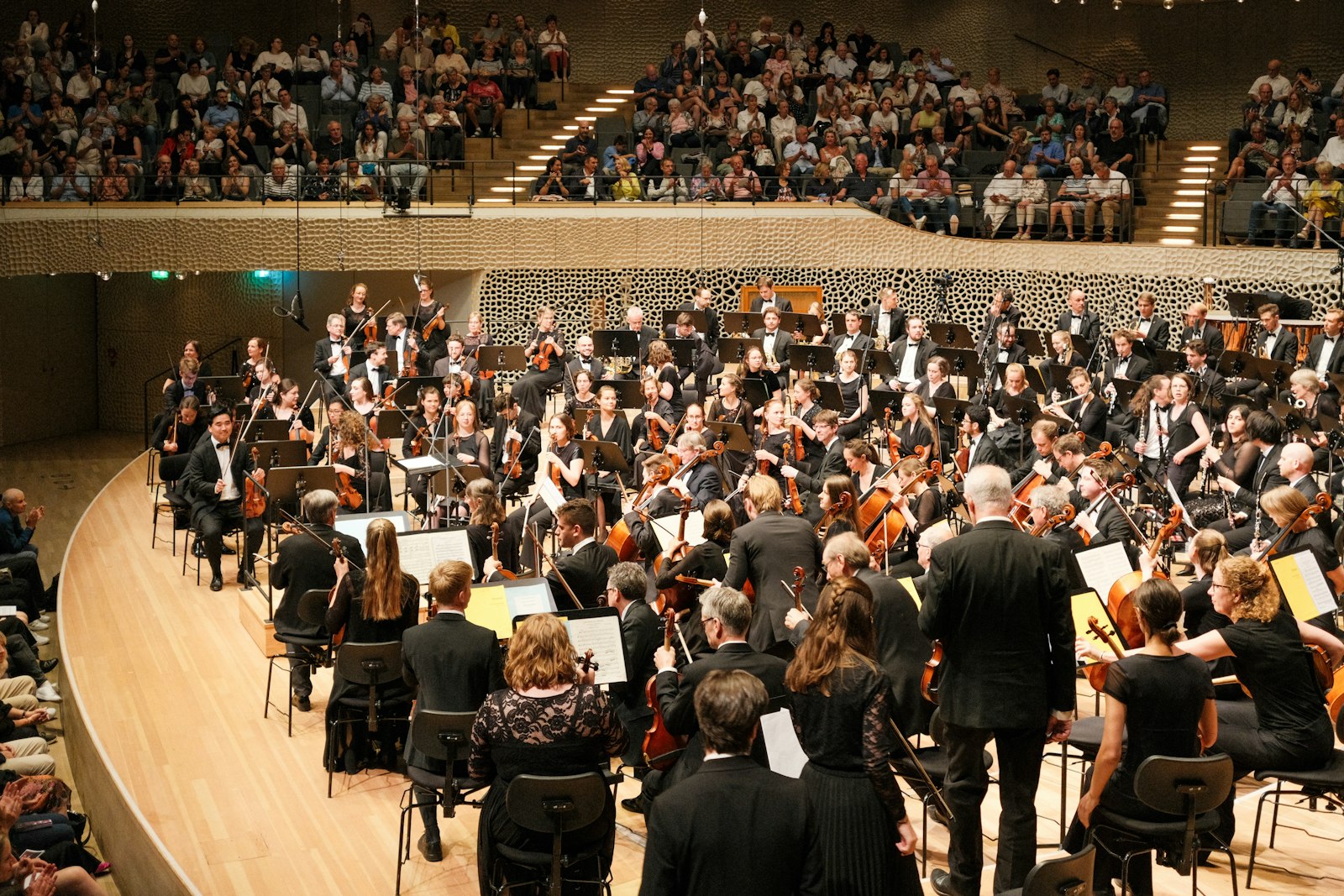 Sinfonieorchester spielt vor vollem Konzertsaal, Blick von der Bühne auf das Publikum