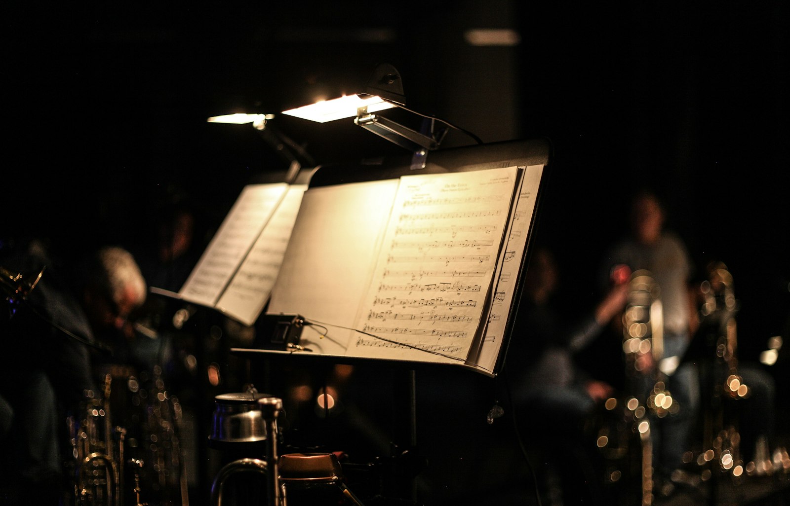 Beleuchtetes Notenpult mit Partitur, im Hintergrund Musiker im Dunkeln