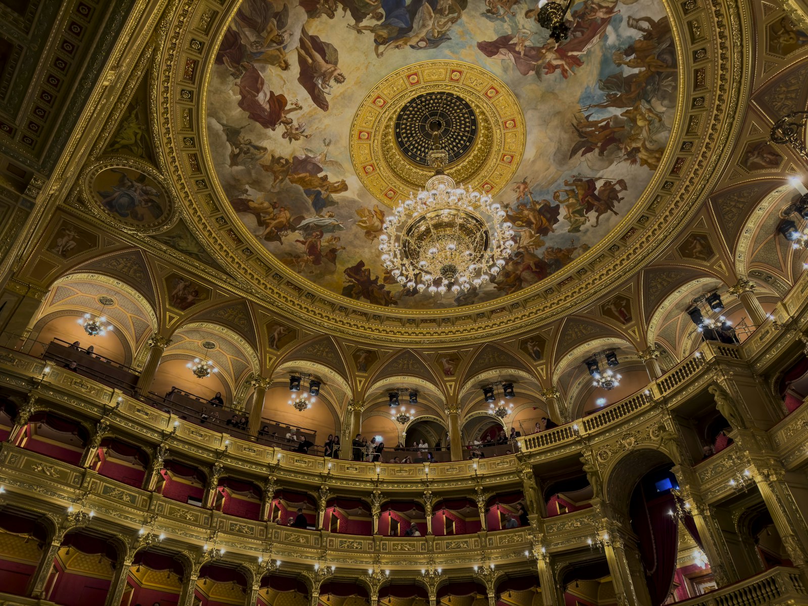 Gilded dome ceiling of a historic opera house with chandelier and tiers of boxes