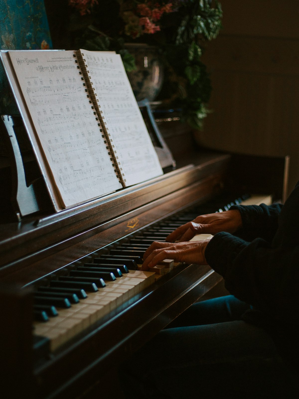 Hände spielen Klavier, im Hintergrund ein aufgeschlagenes Notenheft